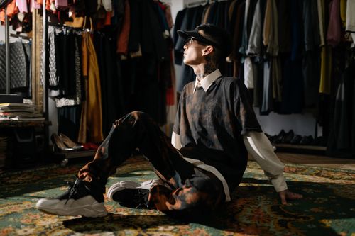 Free Young man in a vintage clothing showroom, seated on a patterned carpet, looking stylish and modern. Stock Photo