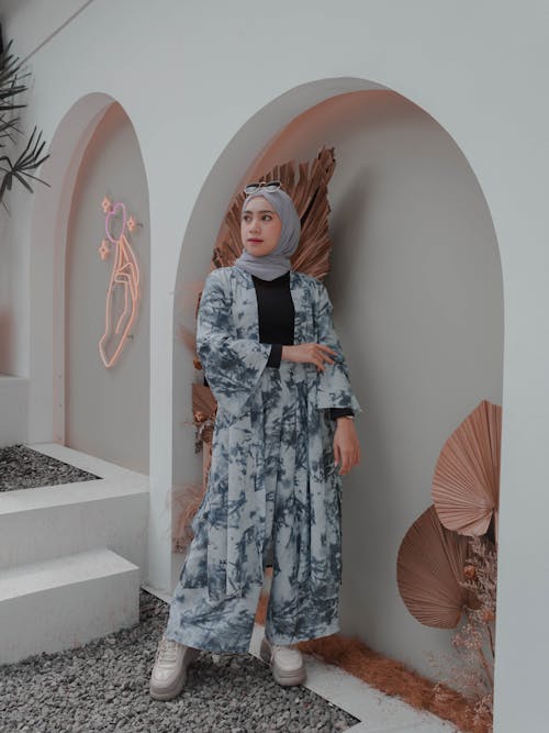 Stylish Muslim woman in hijab standing near arched wall