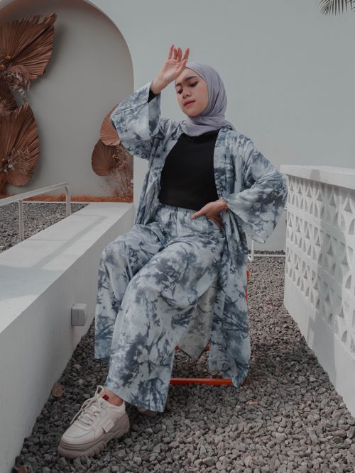 Free Full body fashionable young Muslim female in headscarf and stylish modest clothes sitting with arm raised and hand on waist on contemporary cottage backyard Stock Photo