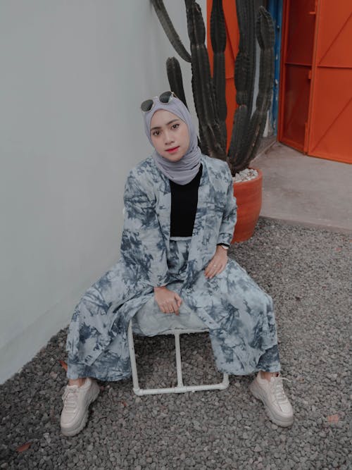 Free Full length confident young Muslim female in hijab and trendy wear sitting on chair on backyard and looking at camera Stock Photo