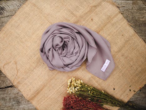 A soft grey scarf elegantly laid on burlap textile, accompanied by delicate dried flowers.