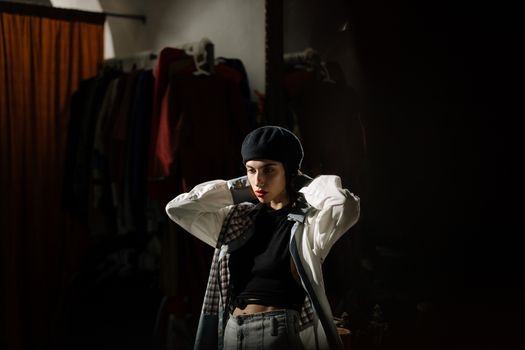 Fashionable woman wearing a beret poses in a clothing store with dramatic lighting.