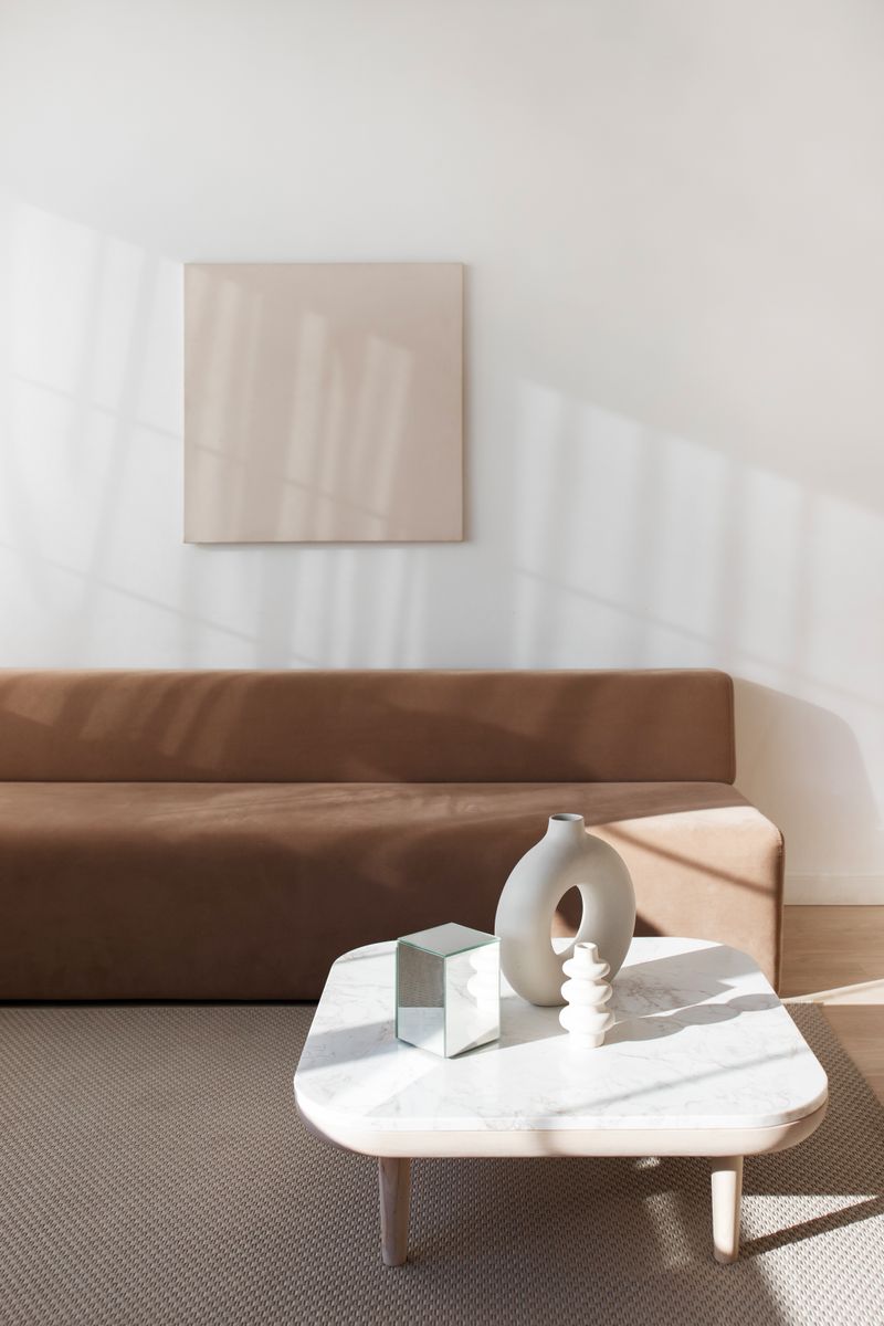 A stylish minimalist living room featuring a brown sofa and modern decor under natural light.