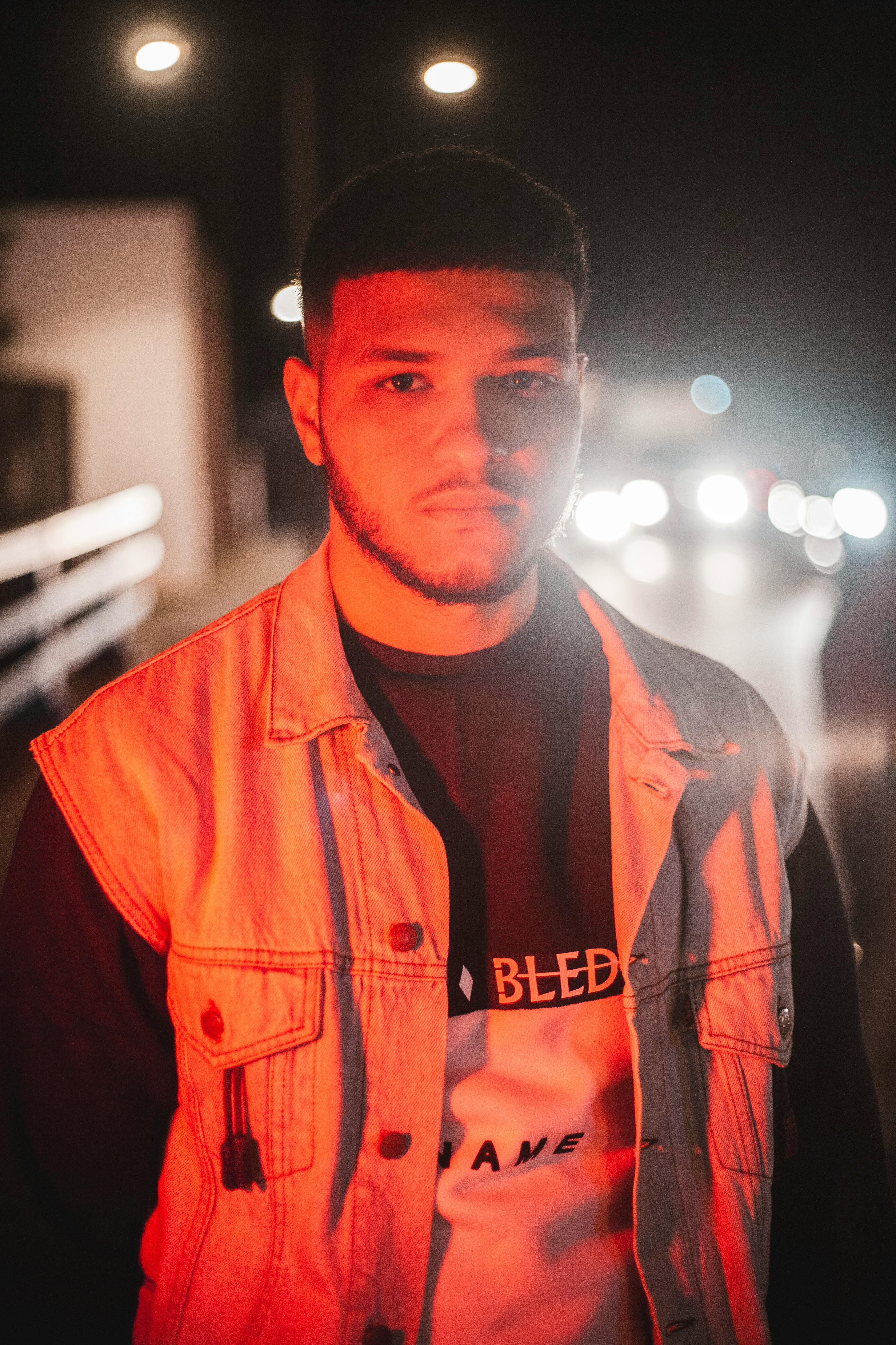 Portrait of a young man in a denim vest with urban street lights at night.