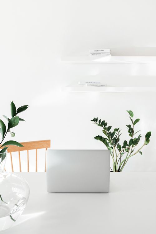 Free A minimalist workspace featuring a closed laptop, houseplants, and a wooden chair on a white desk. Stock Photo