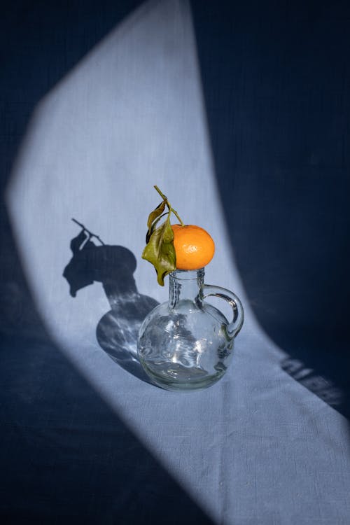 Free Composition of sweet ripe mandarin placed on transparent decanter on blue surface in bright sunlight Stock Photo