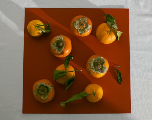 From above arrangement of ripe juicy persimmons and mandarins arranged on brown background on table in light studio