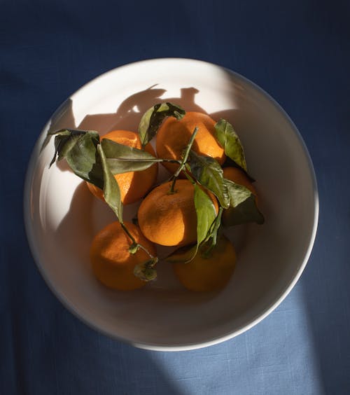 Delicious mandarins heaped in bowl on blue surface
