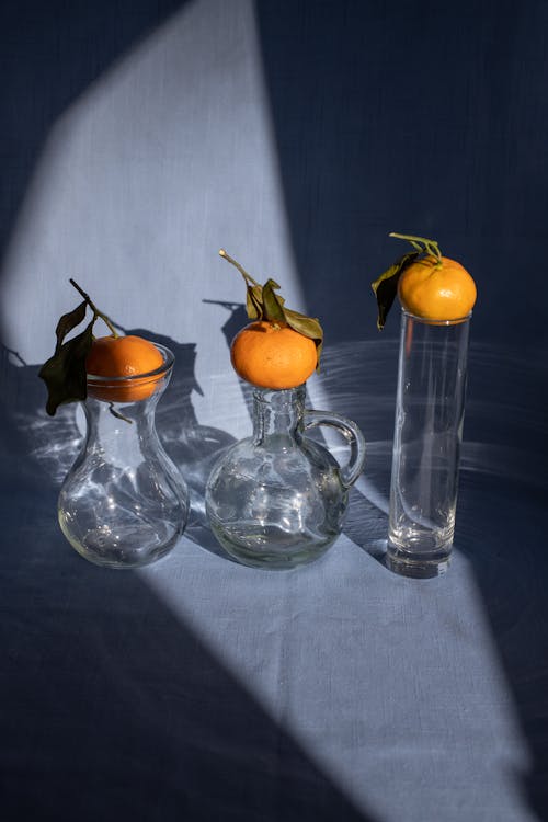 Creative composition of ripe organic mandarins placed on glass vases on blue surface in sunlight