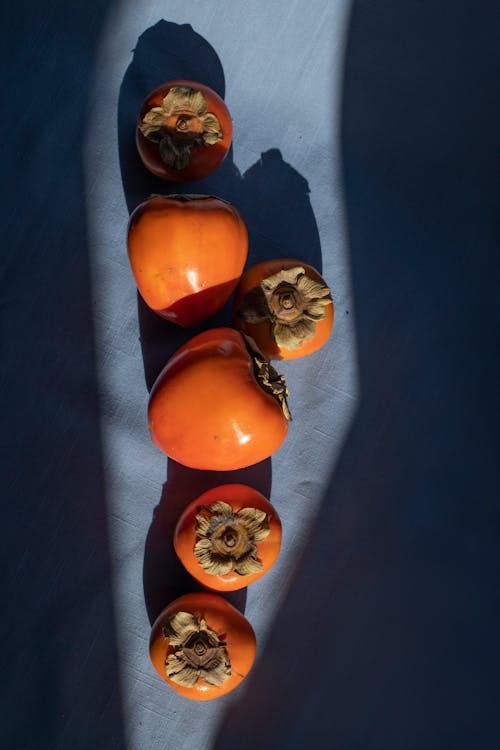 Top view composition of sweet ripe persimmons heaped on dark blue fabric background in sunlight