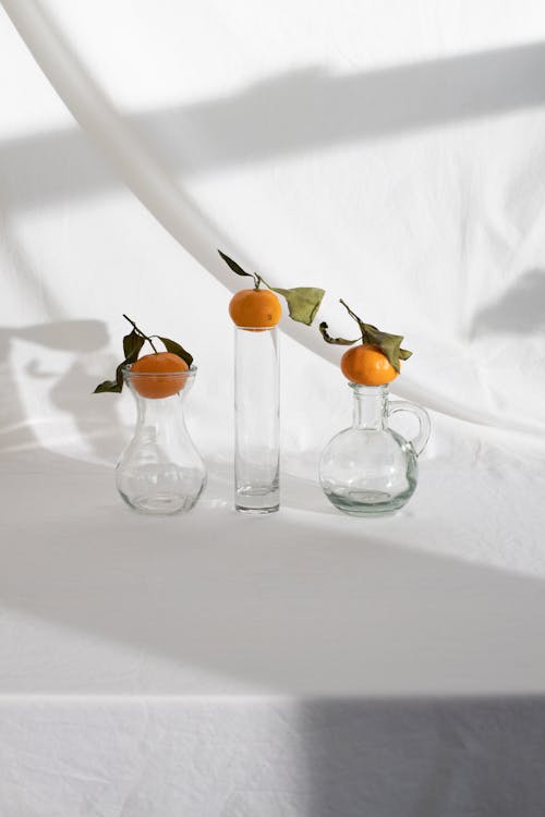 Creative arrangement of ripe juicy mandarins placed on glass vases on white fabric background in light studio