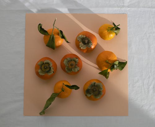 Top view arrangement of sweet persimmons and juicy tangerines placed on pink sheet on table in light room