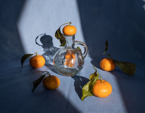 Free From above of fresh ripe tangerines with leaves placed on white tablecloth and composed with glass pitcher in daylight Stock Photo