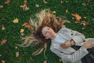 From above of charming female in trendy clothes relaxing on field with closed eyes in autumn park