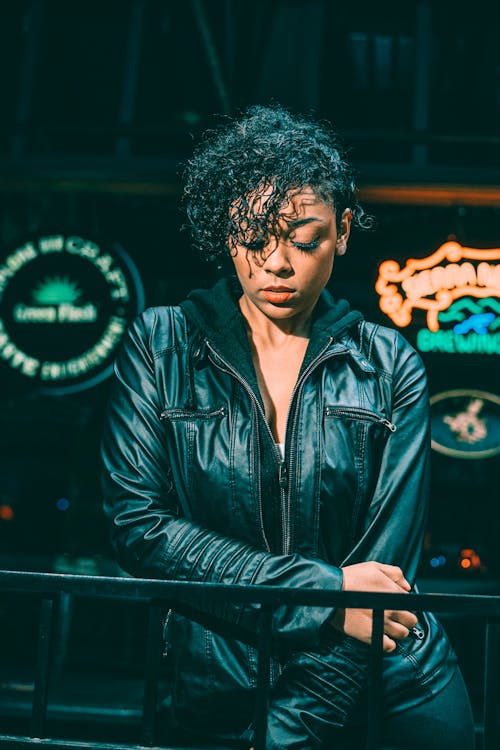 Serious ethnic woman in leather jacket standing near neon signboard