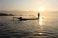 日出时分，一名孤独的渔夫在狭窄的船上保持平衡，向宁静的湖面撒网