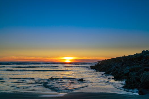 A captivating sunset at Ocean Shores, Washington with gentle waves and rocky shoreline.
