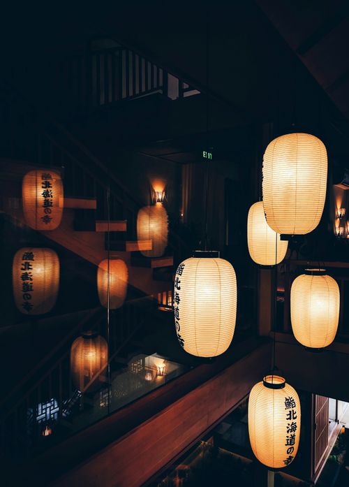 Free A collection of traditional Japanese lanterns illuminating a dimly lit interior space with reflections on the glass. Stock Photo