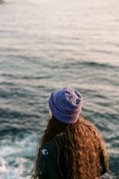 Woman in a beanie looking at the serene ocean, capturing a moment of tranquility.