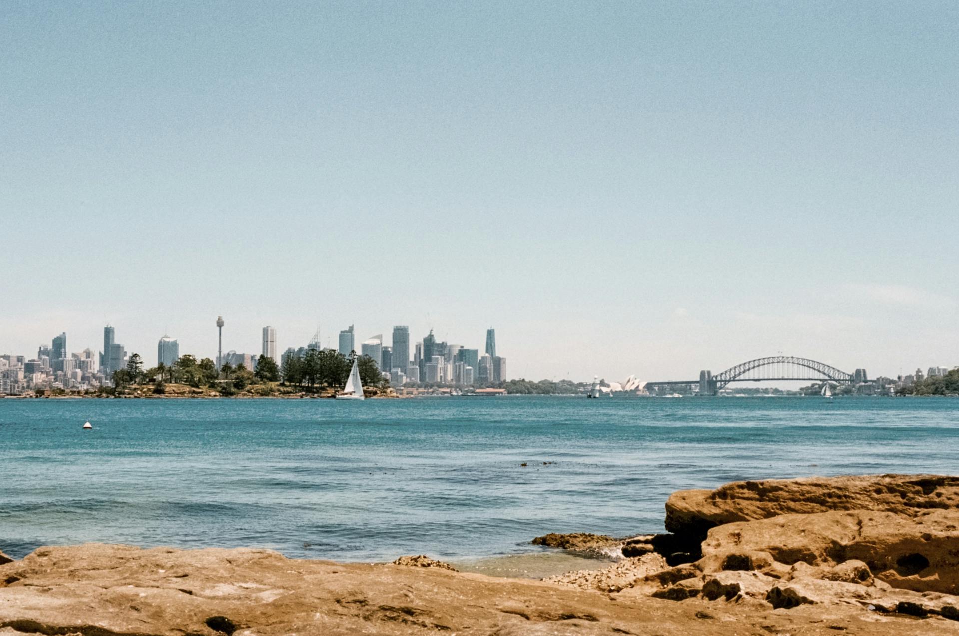 Stunning day view of Sydney Harbour with the city skyline and a sailboat in the foreground.