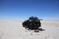 A SUV on the vast Uyuni Salt Flats with travelers during an off-road adventure.