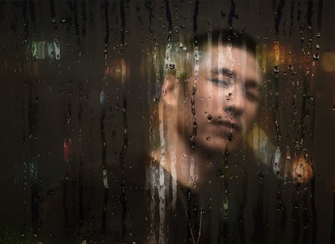 A moody portrait of a man behind a rain-soaked window with blurred city lights.