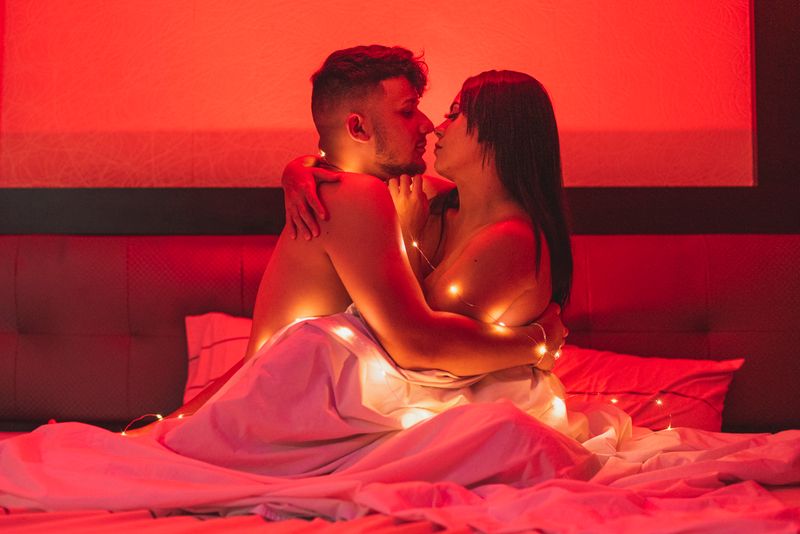 Passionate couple embracing under a warm red glow, wrapped in string lights for a cozy intimate atmosphere.