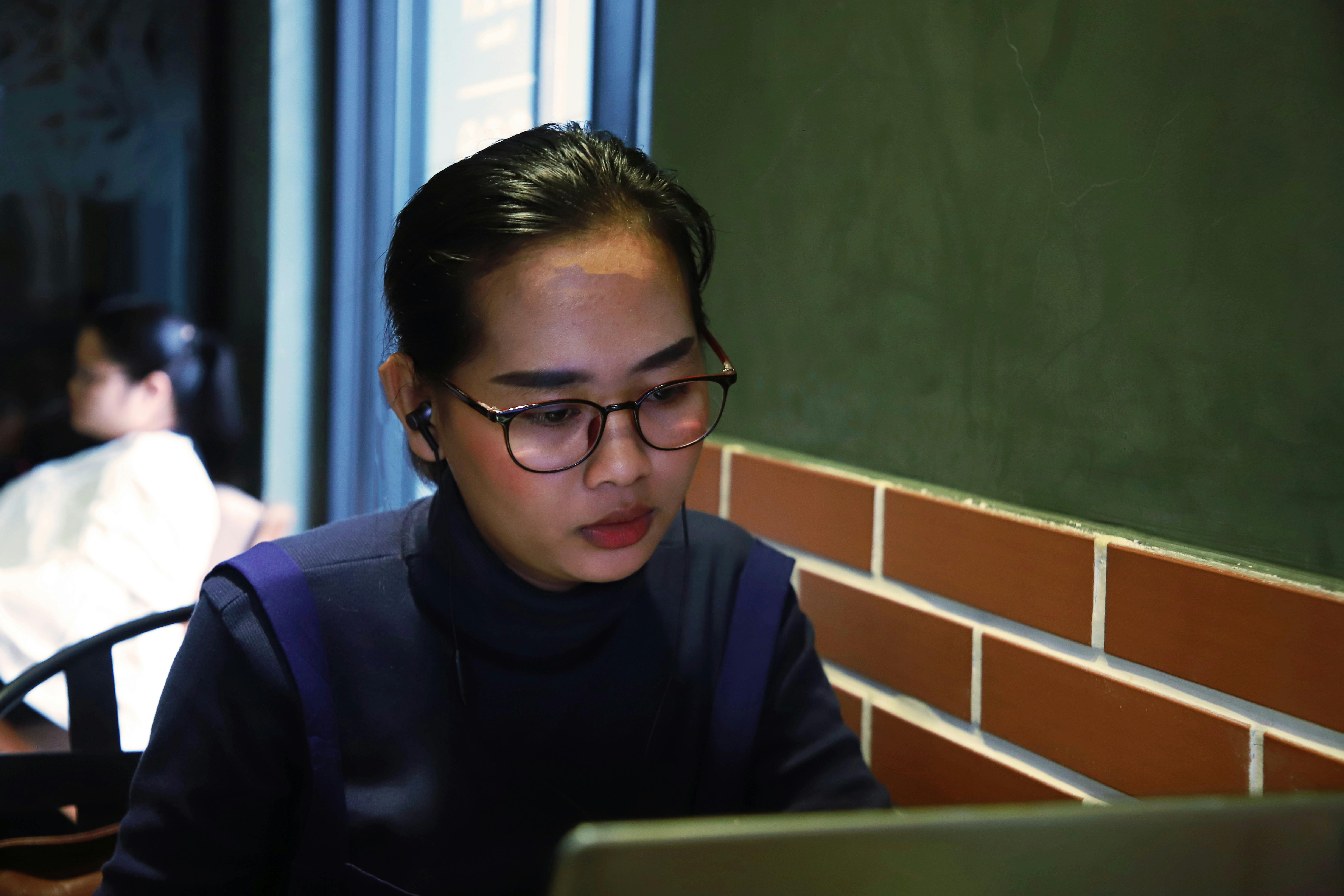 Asian woman focused on laptop for remote work indoors in Cambodia cafe.