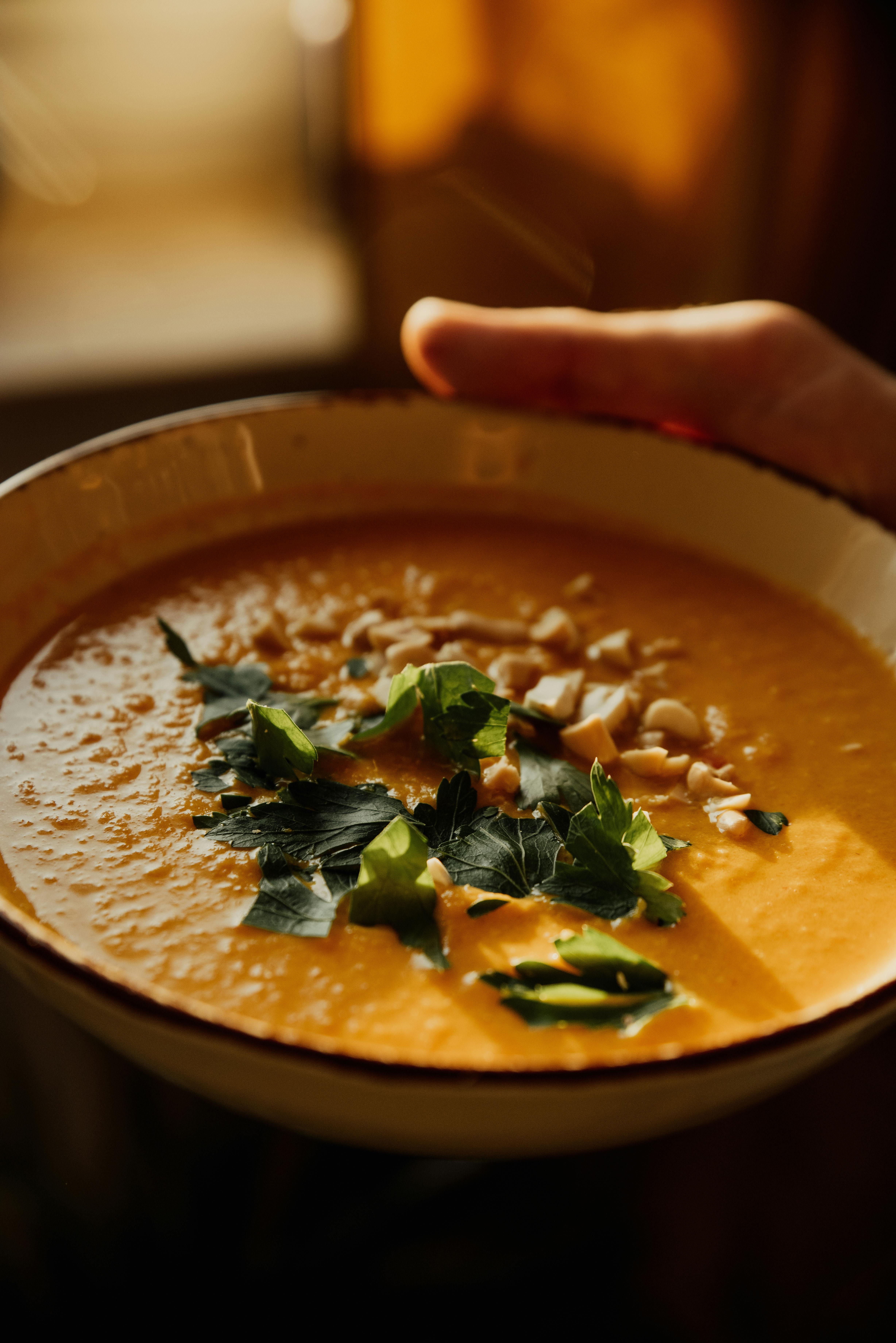 Warm pumpkin soup garnished with nuts and herbs, captured in a ceramic bowl for a cozy culinary presentation.