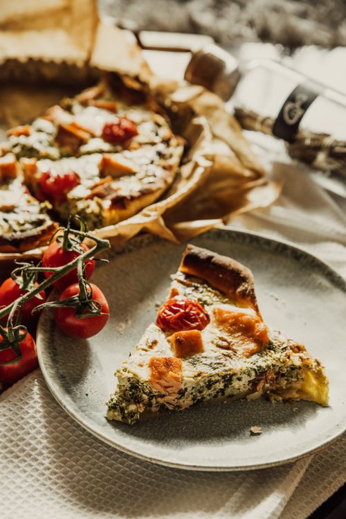 Free Close-up of appetizing spinach quiche garnished with tomatoes and cheese on a plate. Stock Photo