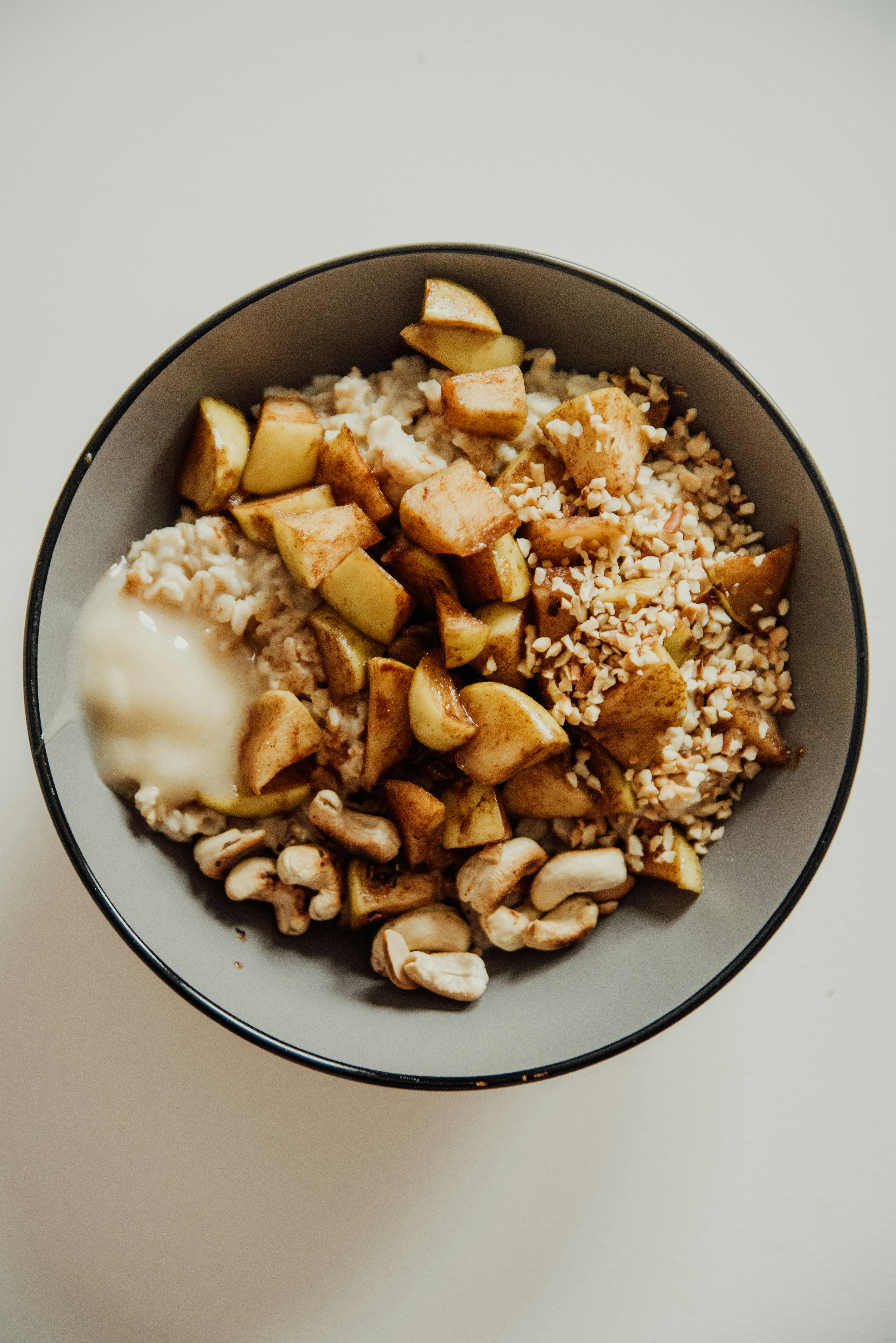 Free Delicious oatmeal bowl with cashews, apples, and honey on a white surface. Stock Photo