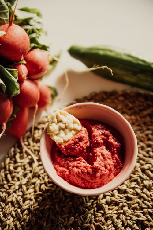 Free Aerial view of a bowl of beetroot hummus with radishes and cucumber on a rustic mat. Stock Photo