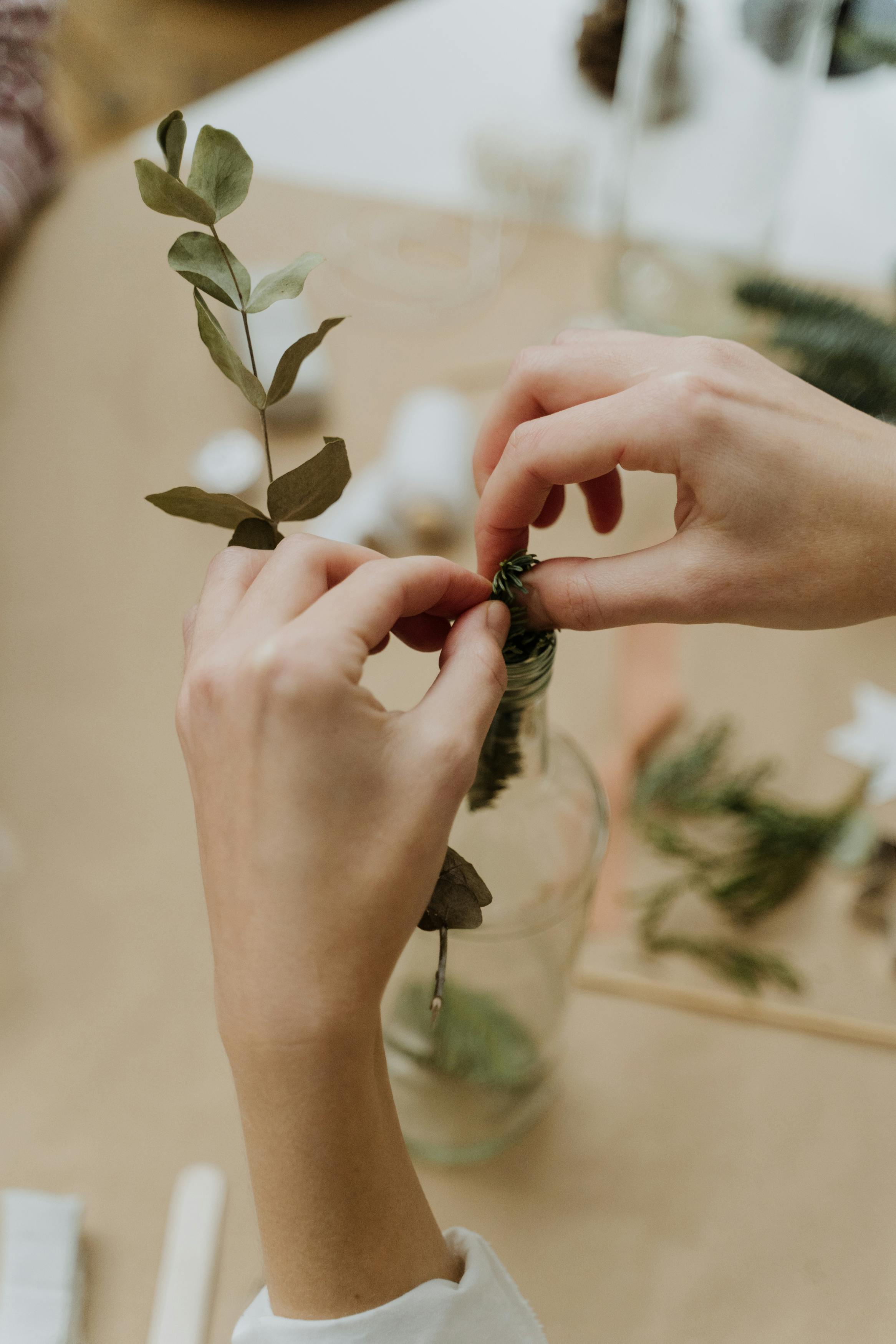 Hands arranging greenery in a clear bottle for a creative decoration project.