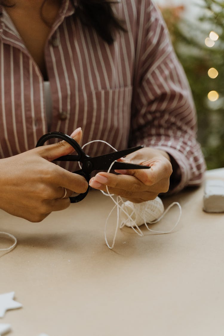 Person In Striped Long Sleeves Cutting A White Yarn 