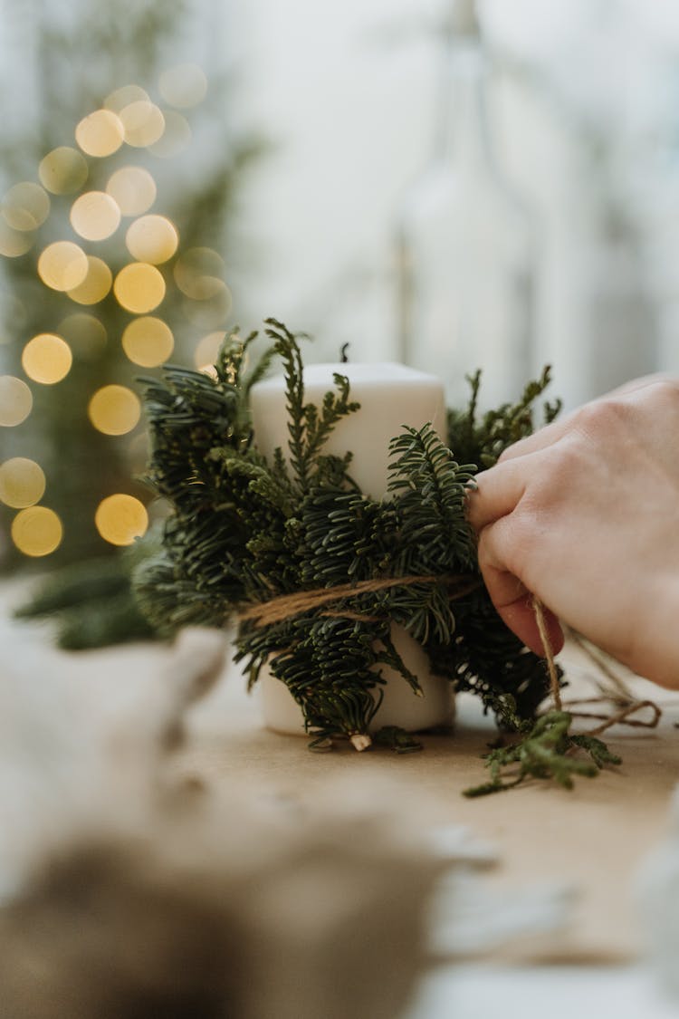 Person Making Christmas Decoration With Candle And Pine Leaves