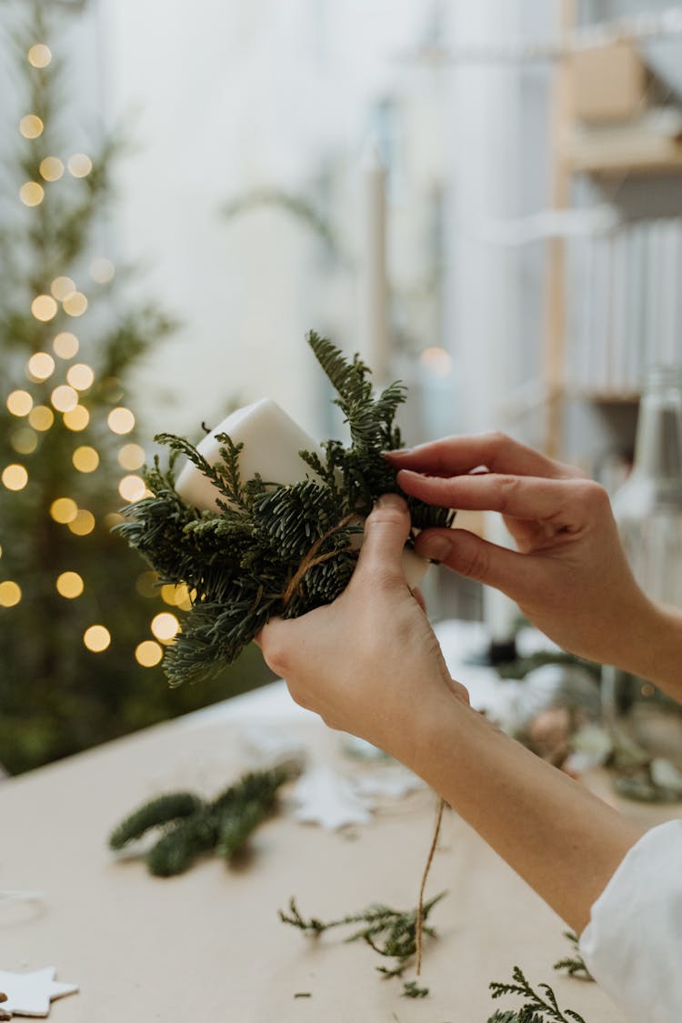 Person Making Christmas Decoration With Candle And Pine Leaves