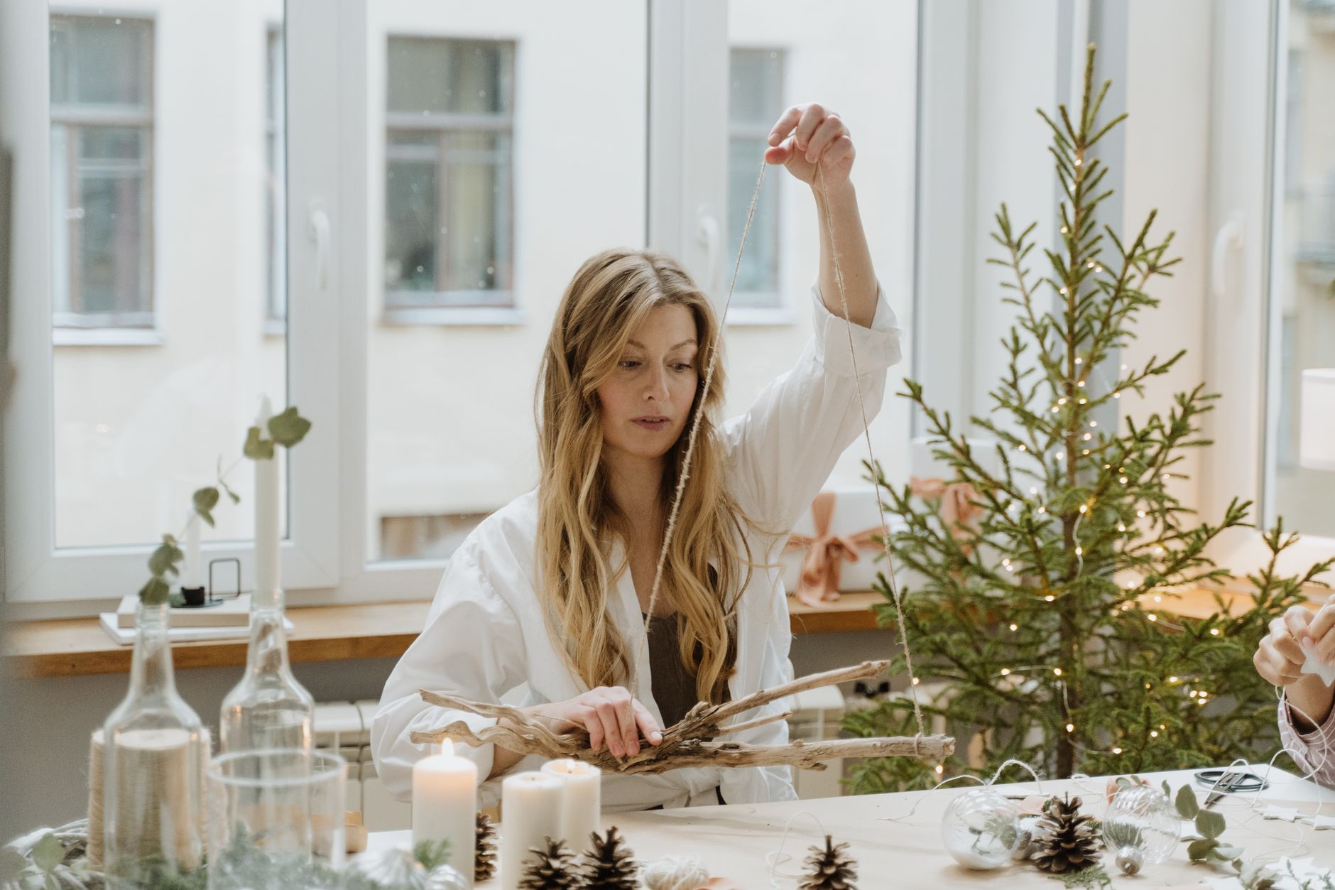 do it yourself crafts for home decor A woman decorates a room for Christmas with handmade ornaments near a small pine tree.