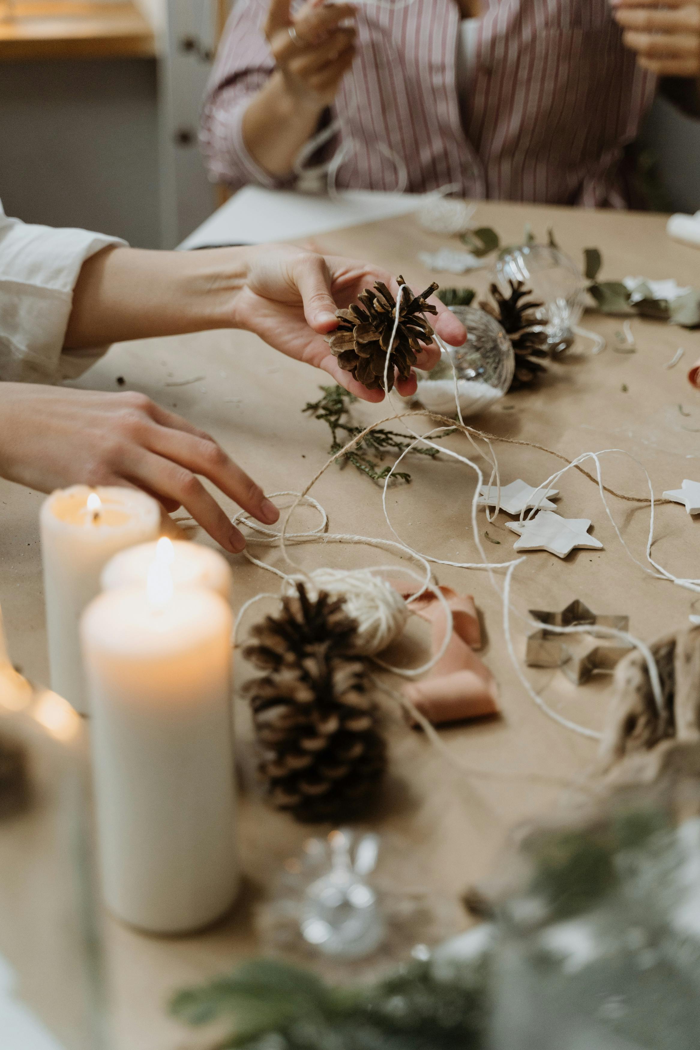 Hands creatively crafting pinecone decorations on a cozy table with candles, perfect for a handmade touch.