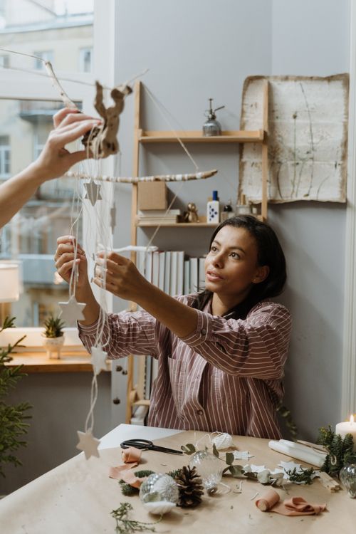 Free Woman creates holiday decoration indoors, crafting a warm and cozy festive atmosphere. Stock Photo