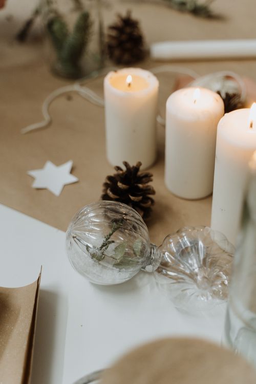 Free Elegant Christmas table decor with lit candles, pine cones, and glass baubles, creating a warm festive atmosphere. Stock Photo