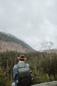 Adult man in a denim jacket sits facing snowy mountains, evoking wanderlust and serenity.