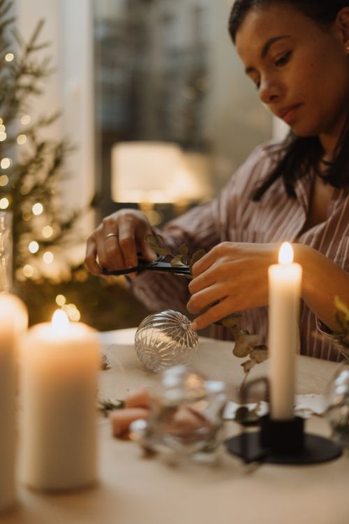 Free A woman engaged in crafting holiday ornaments by candlelight, creating a warm and cozy atmosphere. Stock Photo