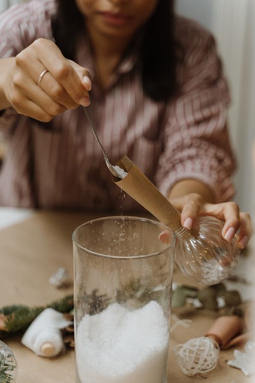 Free Woman creating DIY Christmas decoration by filling a glass bauble with sugar. Stock Photo
