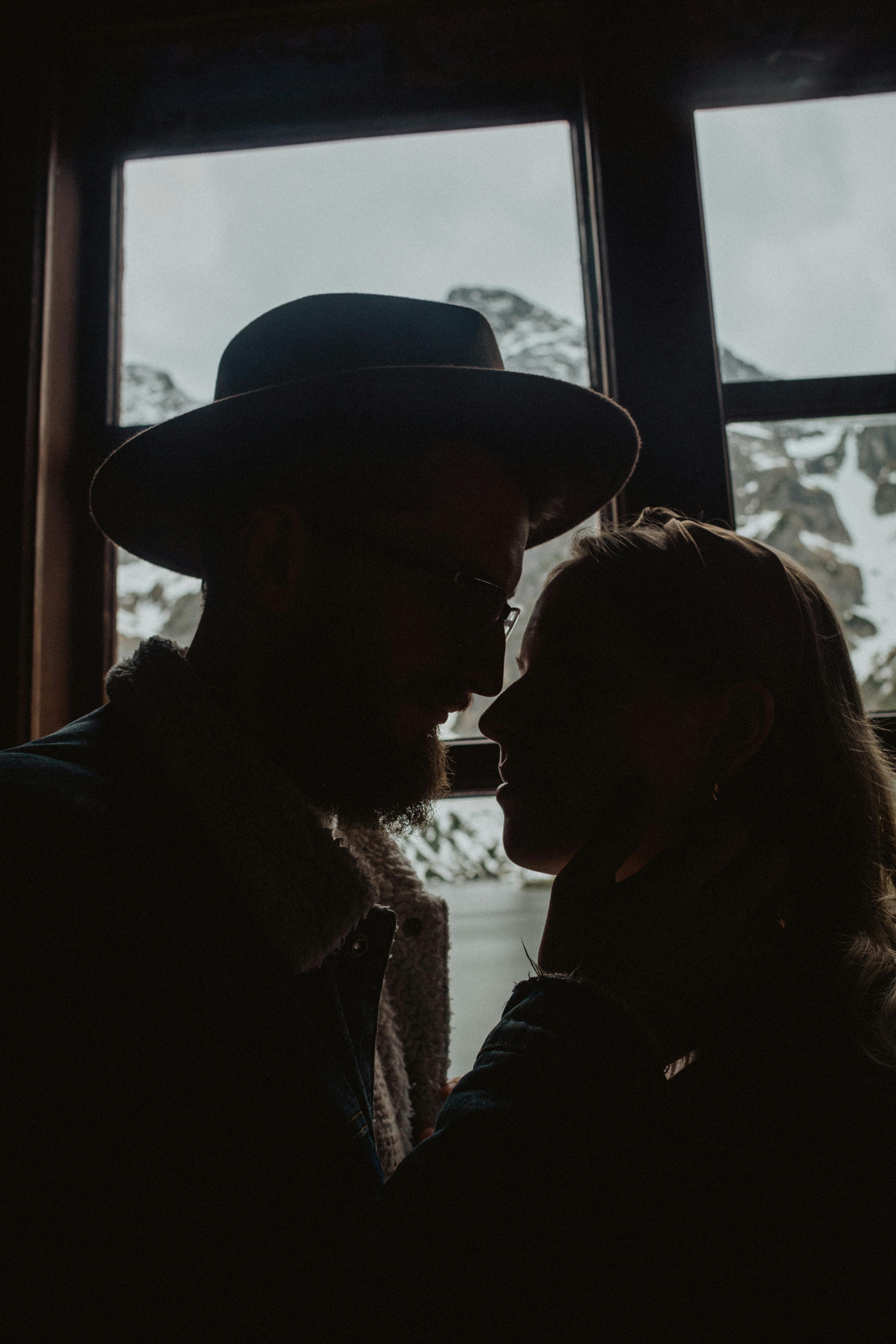 Silhouette of a couple sharing a tender moment by a window with a scenic view outside.