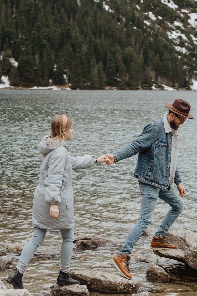 Man And Woman Stepping On Rocks To Cross A Lake