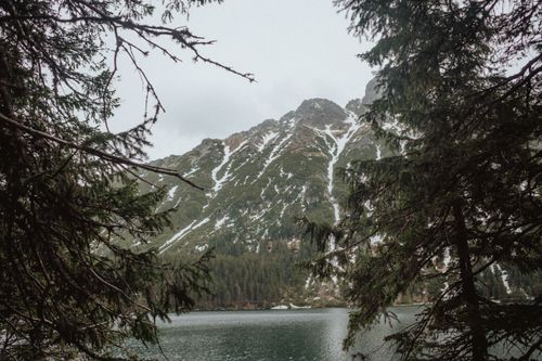 Free Capture serene nature with a stunning mountain lake surrounded by snowy peaks and dense forest. Stock Photo