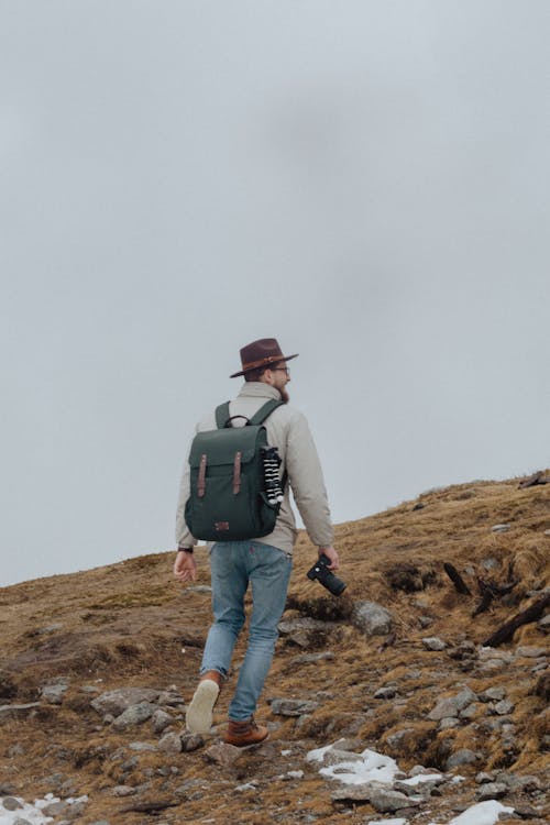 Man in Gray Jacket With Backpack and Camera Hiking Under Gray Sky