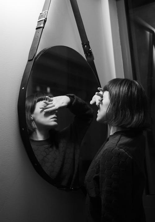 Grayscale Photo of a Woman Standing in Front of a Mirror