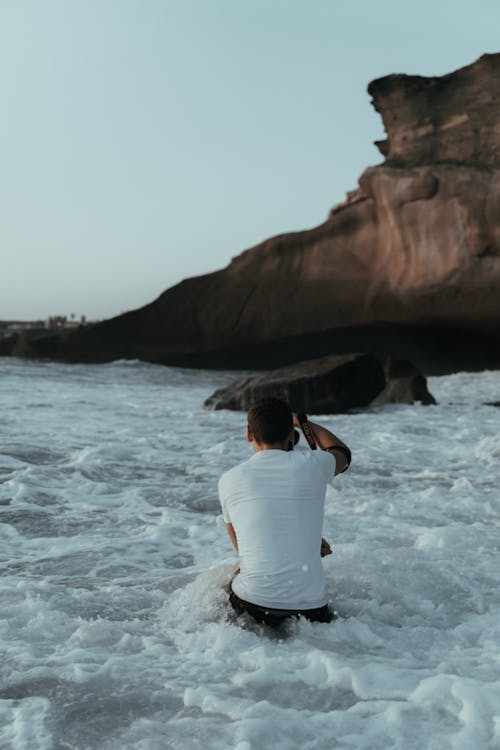 A Photographer Taking Photos of a Rock Formation at a Beach