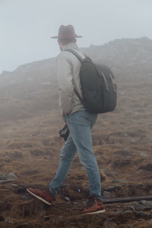 Man in Gray Jacket and Blue Denim Jeans Standing Near a Mountain